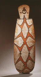 Ovale Asmat schild, gesneden in reliëf met gestileerde figuren, een masker bovenaan