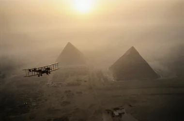 Het vintage vliegtuig Vimy vliegt boven mistige piramides tijdens een gouden zonsopgang