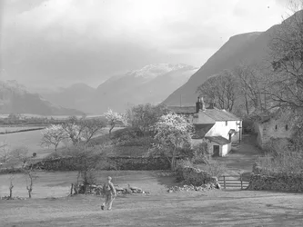 Een man loopt in de richting van een laan en Gillerthwaite House, met het meer en de bergen op de achtergrond
