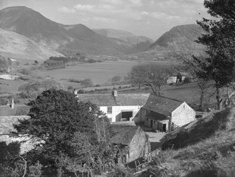 Gezicht op wat een boerderij lijkt te zijn op de voorgrond en een meer en heuvels op de achtergrond