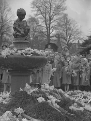 Kinderen plaatsen bosjes narcissen op fontein met standbeeld erop
