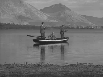 Drie mannen in een roeiboot op een meer aan het vissen, één man is zee; zeegezicht;geted, bergen op achtergrond