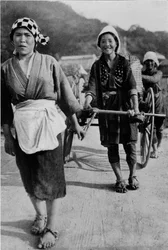 Drie generaties vrouwen duwen een kar met grootmoeder achteraan, ca. 1900, 1921