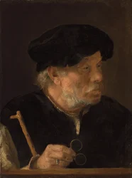 Een man, buste-lengte, met een wandelstok en zijn bril, bij een houten rand