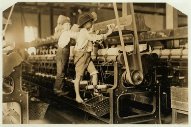 Kleine jongens klimmen op spinmachine om gebroken draden te repareren en lege spoelen te vervangen bij Bibb Mill, Macon, Georgia, 1909