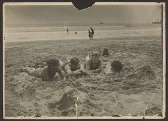 [Kinderen liggen in het zand op het strand].