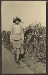 [Vrouw loopt langs hek met bloemen].