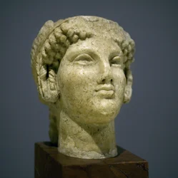 Meisjeshoofd (Kore), sculptuur uit de Romeins-Hellenistische periode (3e-2e eeuw na onze jaartelling), zeer expressief gezicht, prominente jukbeenderen naar het oosten, glimlach, krullend haar, archaïsche stijl van Ionië in de 6e eeuw voor onze jaartelling
