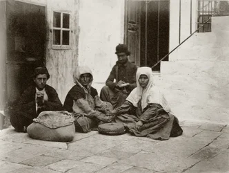 Vrouwen die meel malen met ronde molenstenen in een binnenplaats van een huis in Jeruzalem