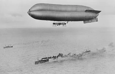 RNAS Coastal Class luchtschip C23A vliegend boven een oorlogsschip konvooi, ca. 1917