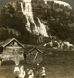 Kinderen die spelen in een boerenveld met terrasvormige Tvinde-waterval, Vossevangen, Noorwegen, ca. 1905