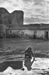 Jong meisje spelend met een papieren bootje in een plas omgeven door modder, Venosa, Basilicata, Italië