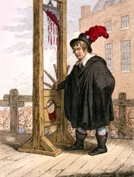 George Tierney verkleed als beul naast een guillotine.