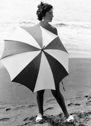 Vrouw met paraplu op strand, ca 1960 (z/w foto)
