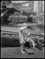 Blootsvoetse jongen, mogelijk William Gray Hassler, speelt met hond aan de oever van een rivier of meer, New York, ca. 1910