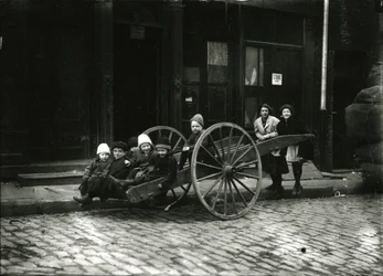 Groep kinderen in kar, met meisje en vrouw staand erachter, ca. 1910-21