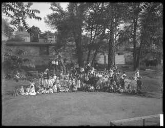 Grote groep kinderen verzameld voor een groepsportret op een onbekend speelterrein, ca. 1910