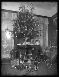 Seymour jongen poseerde met driewieler naast kerstboom in salon, Kerstmis 1912