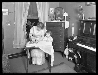Ongeïdentificeerde vrouw demonstreert het gebruik van een elektrisch strijkijzer, bekeken door een klein meisje, c.1913-14