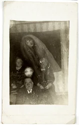 Paranormaal fenomeen: portret van drie oude mensen, de geest van een vrouw die achter hen verschijnt, circa 1920